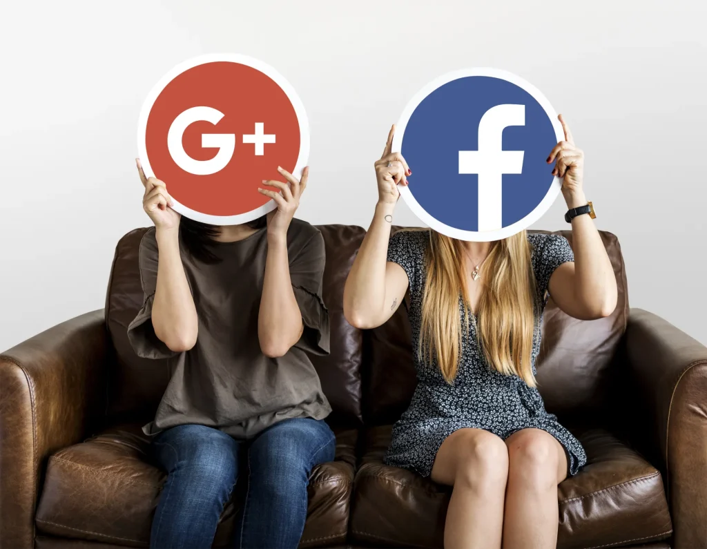 Due donne sedute su un divano tengono davanti al viso cartelli con i loghi di Google Plus e Facebook.